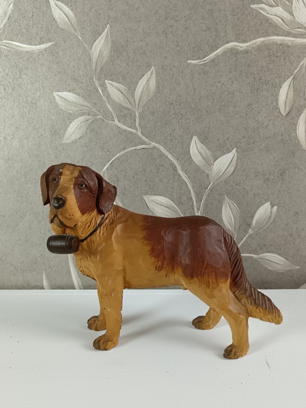 A carved and painted wooden sculpture of a standing Saint Bernard dog wearing a barrel around its neck.