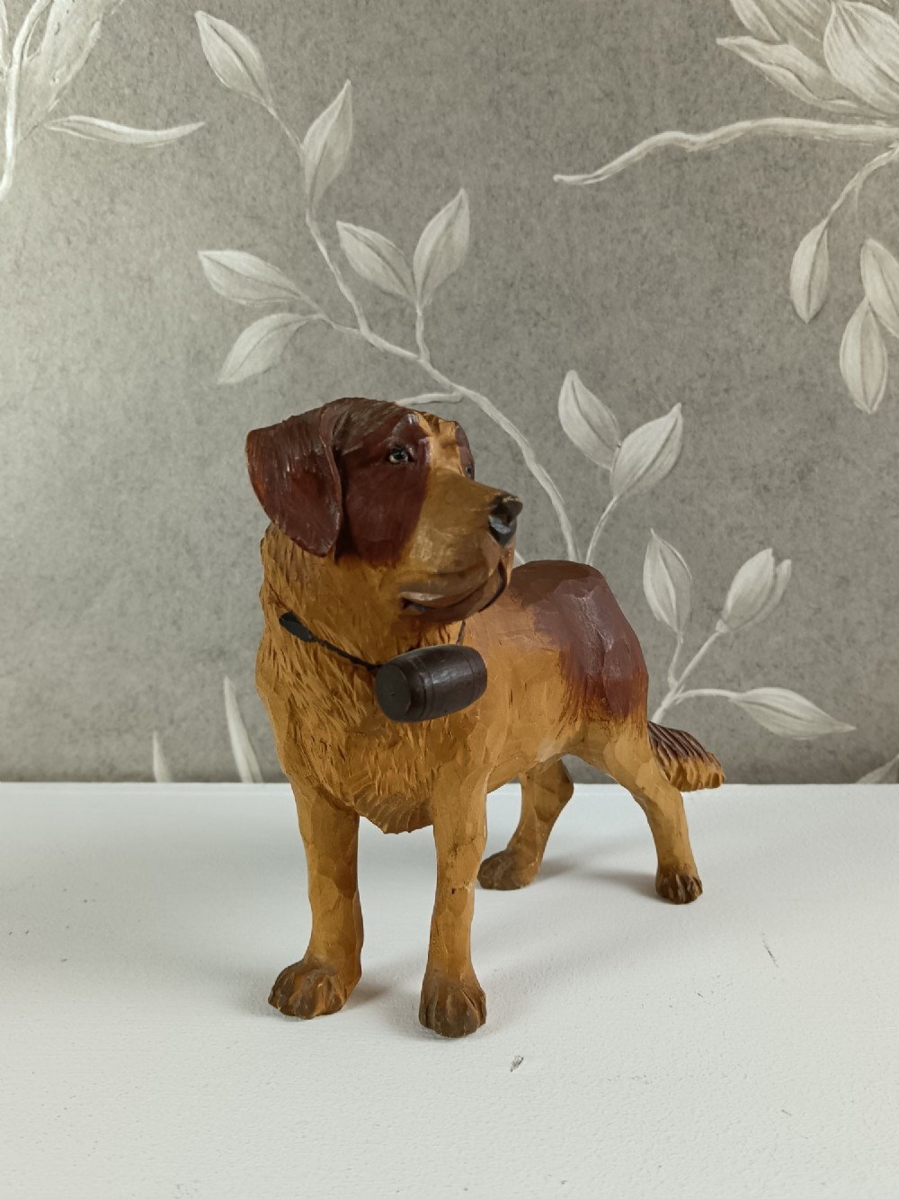 A carved and painted wooden sculpture of a standing Saint Bernard dog wearing a barrel around its neck. View IX