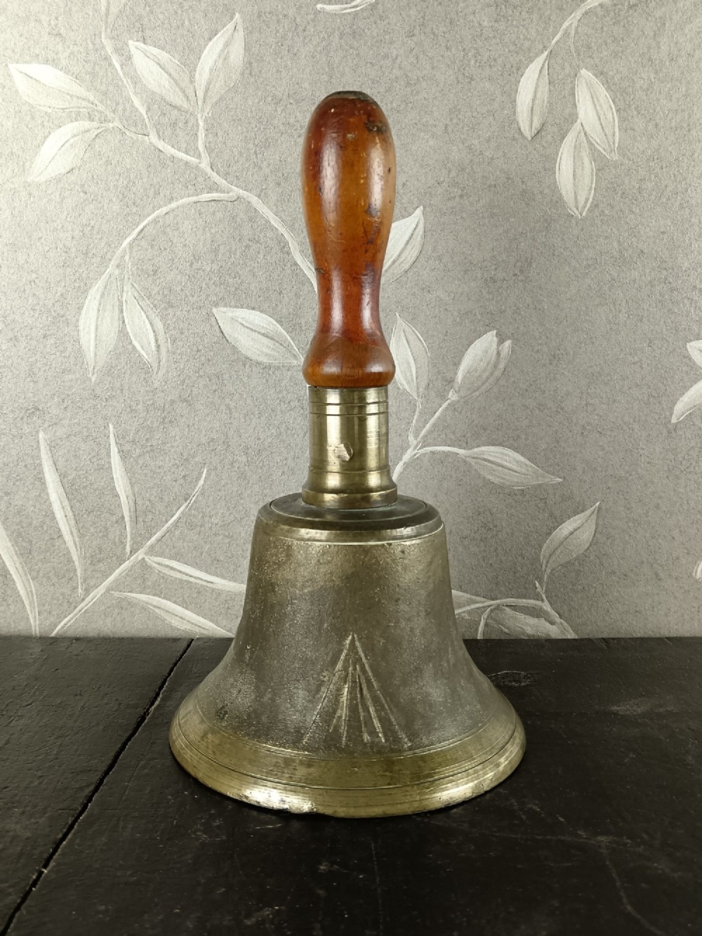 A cast brass military handbell featuring an engraved broad arrow mark and a turned dark wood handle.