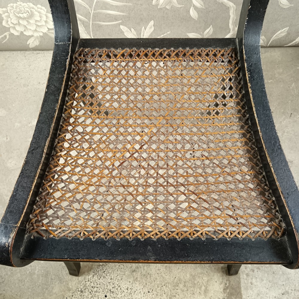 An ebonised Regency side chair featuring curved sabre legs, a woven cane seat, turned top rail, and a carved back splat with brass detail. View VII