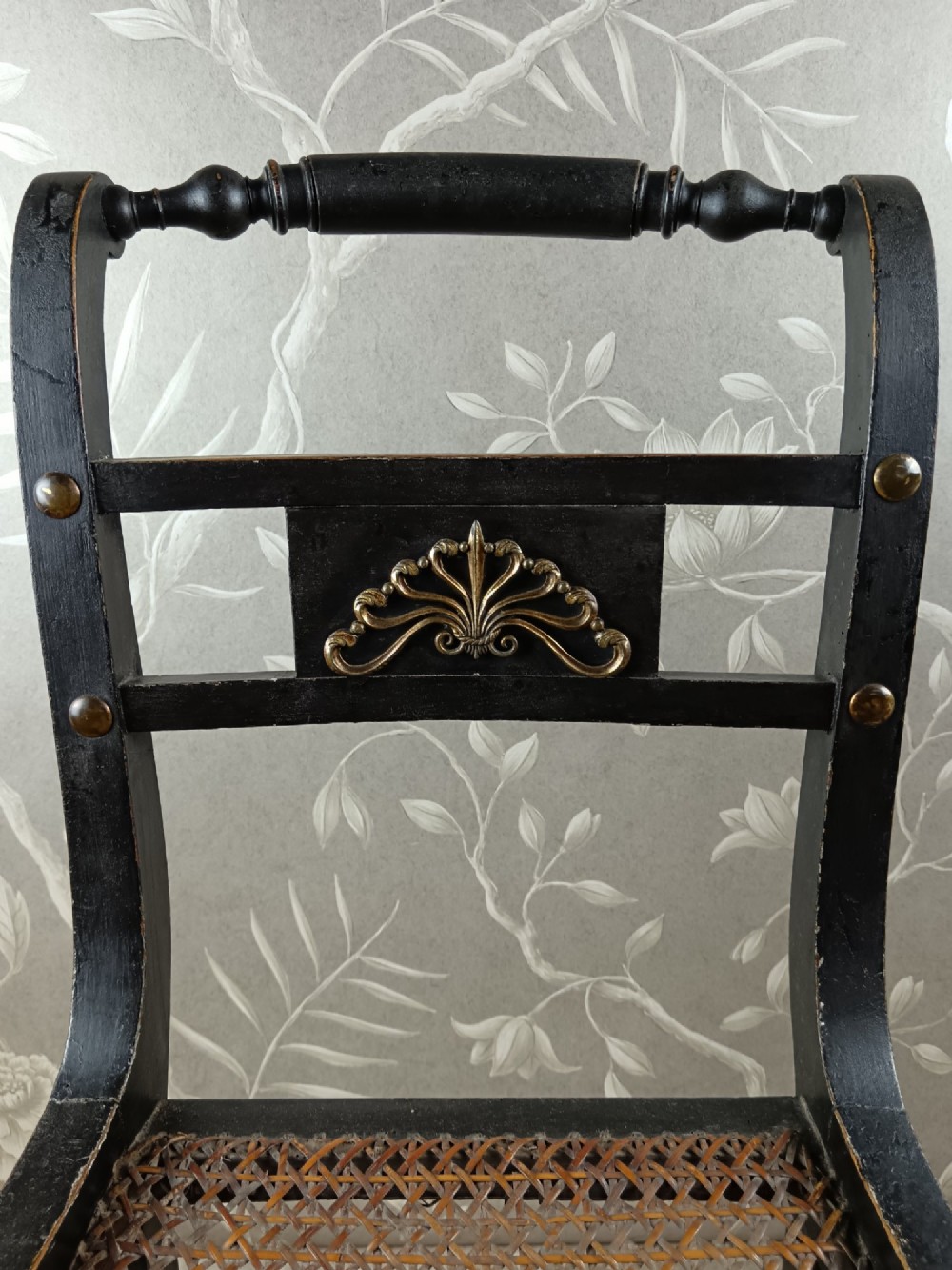 An ebonised Regency side chair featuring curved sabre legs, a woven cane seat, turned top rail, and a carved back splat with brass detail. View IX