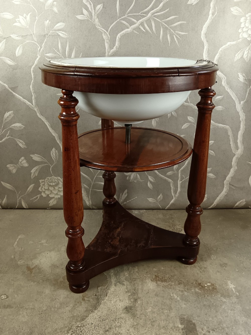 A 19th-century circular mahogany campaign washstand featuring three turned legs, a circular tier, a triangular platform base, and an inset white ceramic wash basin. View II