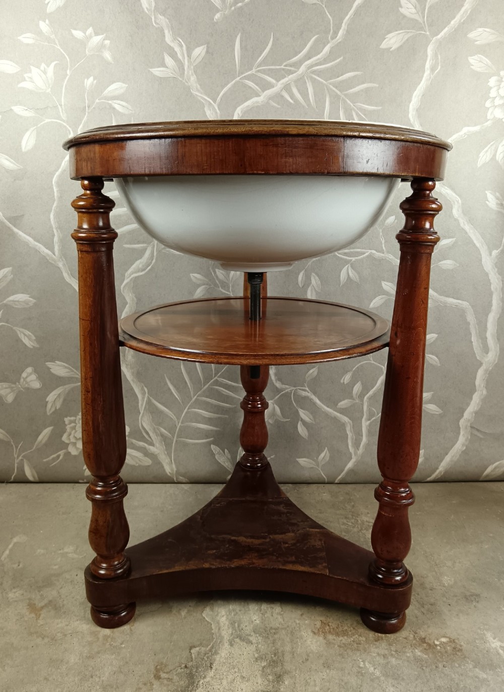 A 19th-century circular mahogany campaign washstand featuring three turned legs, a circular tier, a triangular platform base, and an inset white ceramic wash basin. View IV