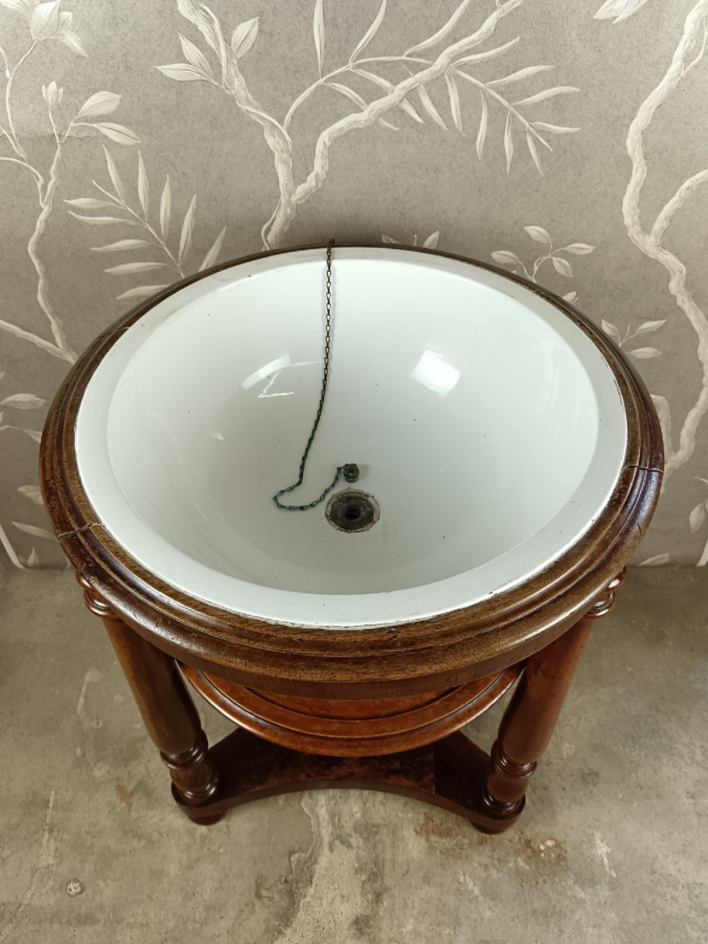 A 19th-century circular mahogany campaign washstand featuring three turned legs, a circular tier, a triangular platform base, and an inset white ceramic wash basin. View V