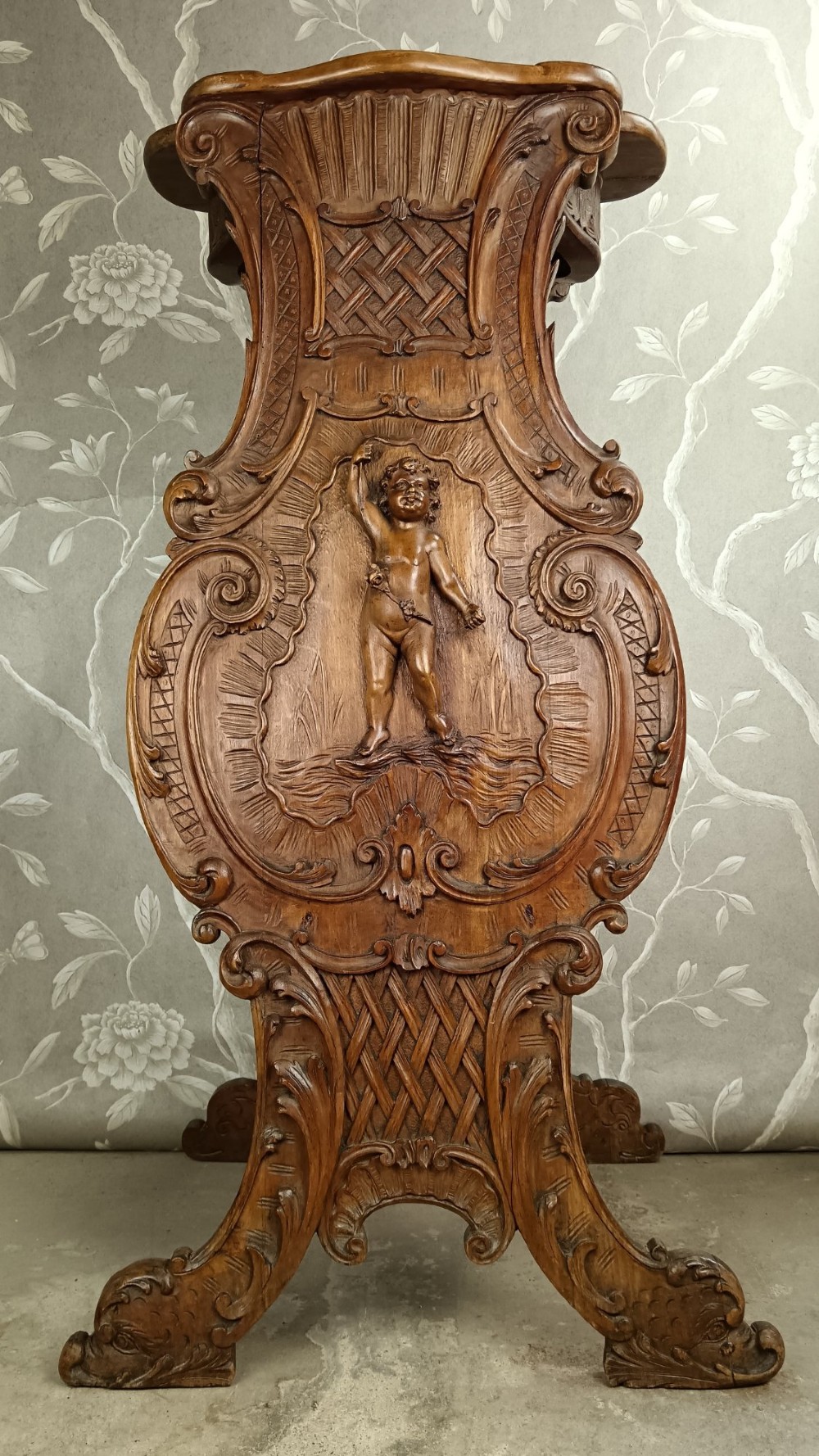 A 19th-century Italian carved walnut pedestal stand featuring a central relief carving of a cherub, acanthus scrollwork, and lattice detailing.