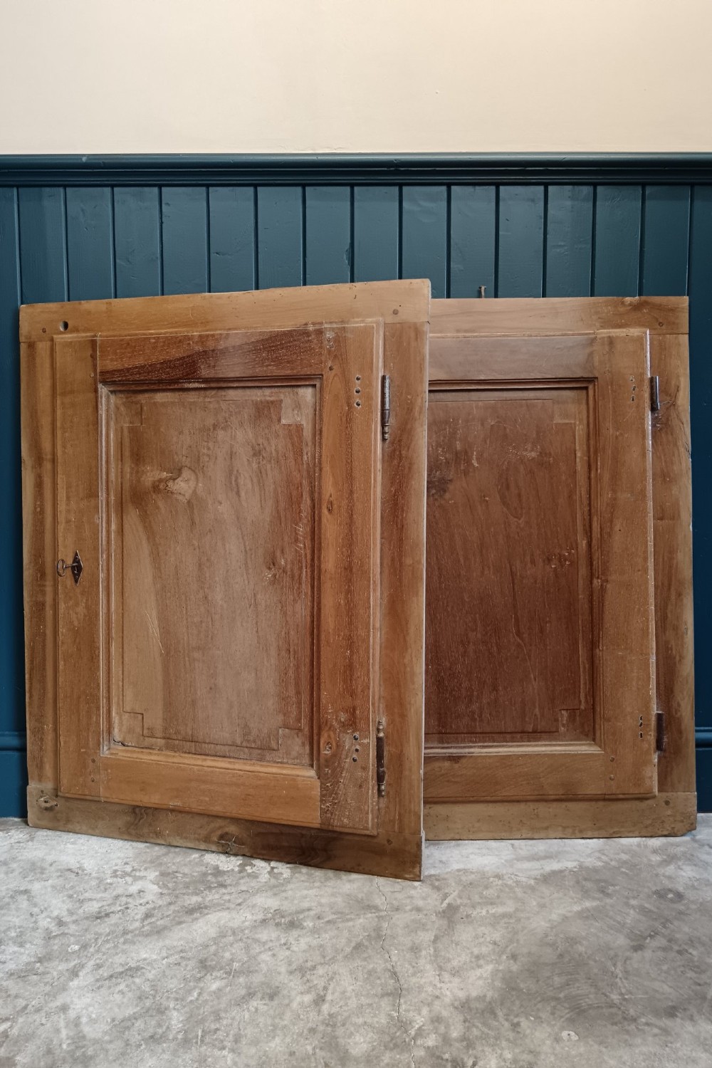 A pair of antique Italian walnut cupboard doors set within rectangular timber frames with recessed panels and iron hardware.