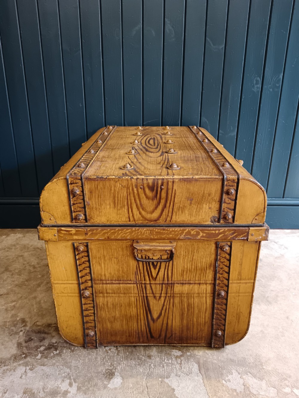 A late nineteenth-century metal steamer trunk featuring a hand-painted faux wood grain finish, dark metal banding, studs, and a central latch. View II