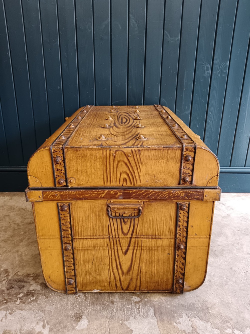 A late nineteenth-century metal steamer trunk featuring a hand-painted faux wood grain finish, dark metal banding, studs, and a central latch. View IV
