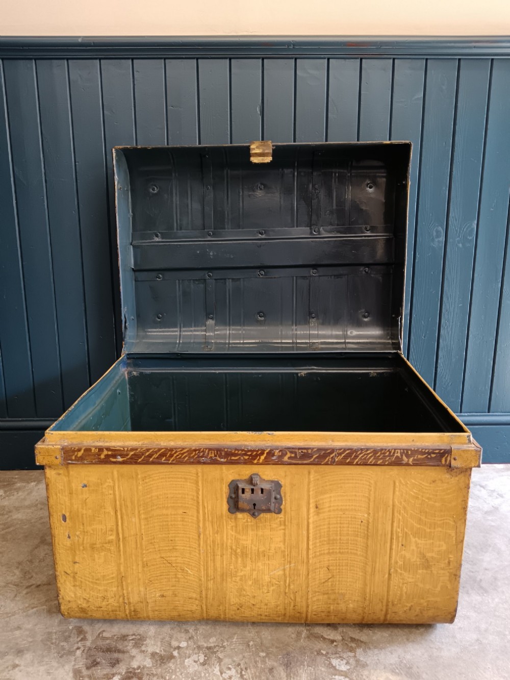 A late nineteenth-century metal steamer trunk featuring a hand-painted faux wood grain finish, dark metal banding, studs, and a central latch. View VI