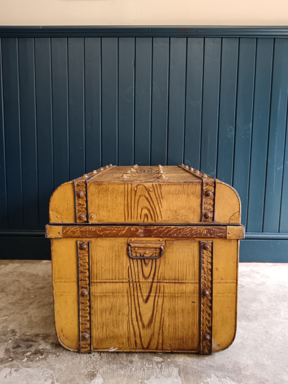 A late nineteenth-century metal steamer trunk featuring a hand-painted faux wood grain finish, dark metal banding, studs, and a central latch. View IX