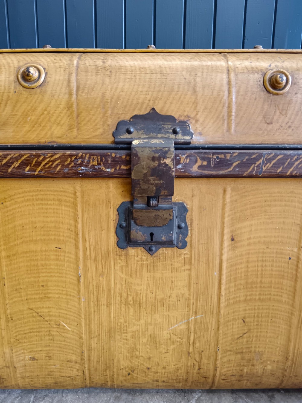 A late nineteenth-century metal steamer trunk featuring a hand-painted faux wood grain finish, dark metal banding, studs, and a central latch. View X