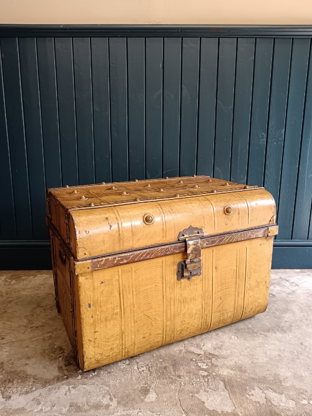 A late nineteenth-century metal steamer trunk featuring a hand-painted faux wood grain finish, dark metal banding, studs, and a central latch. View XIII