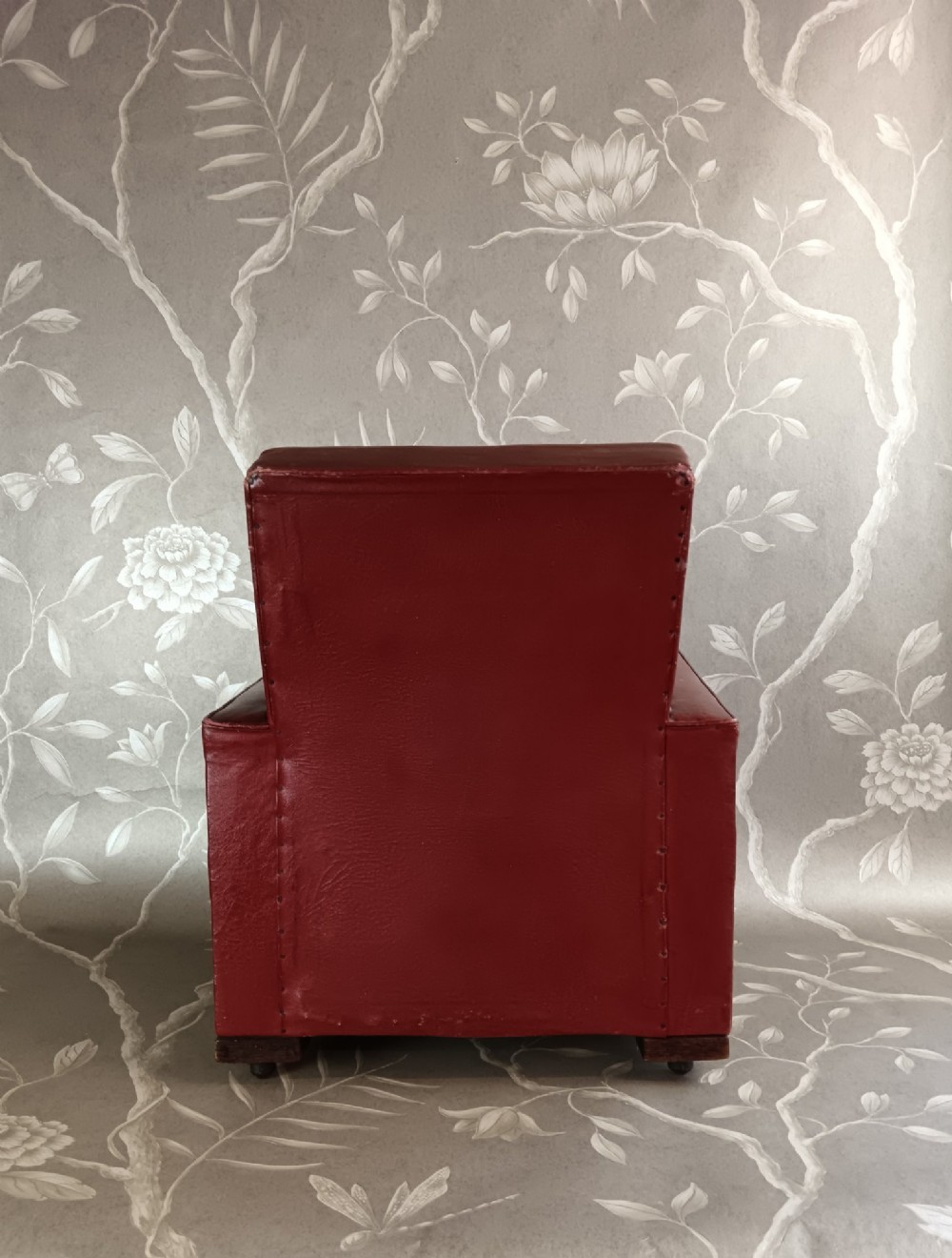 A child-sized 1930s Art Deco club chair upholstered in oxblood red leather with studded trim along the arms. View V