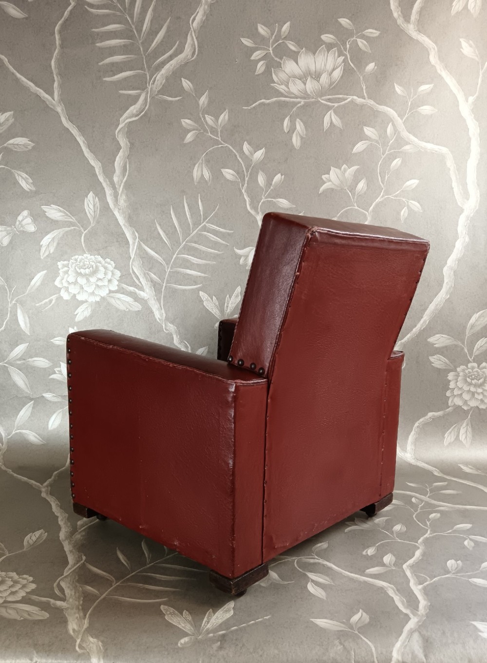 A child-sized 1930s Art Deco club chair upholstered in oxblood red leather with studded trim along the arms. View VI