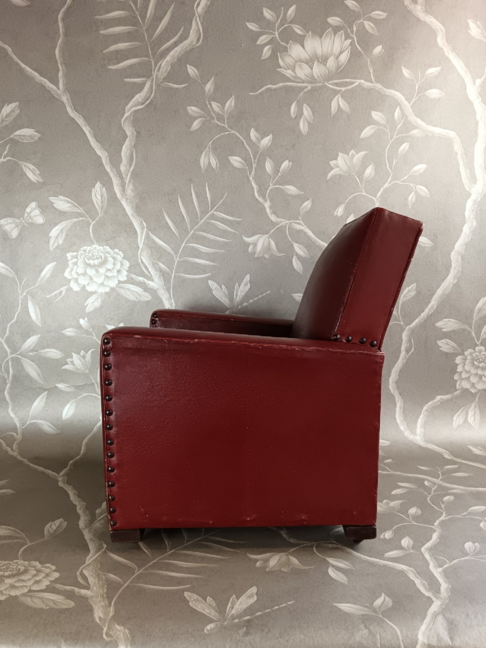 A child-sized 1930s Art Deco club chair upholstered in oxblood red leather with studded trim along the arms. View VII
