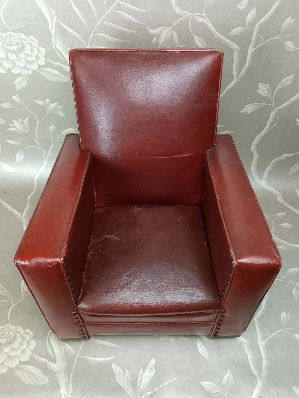A child-sized 1930s Art Deco club chair upholstered in oxblood red leather with studded trim along the arms. View IX