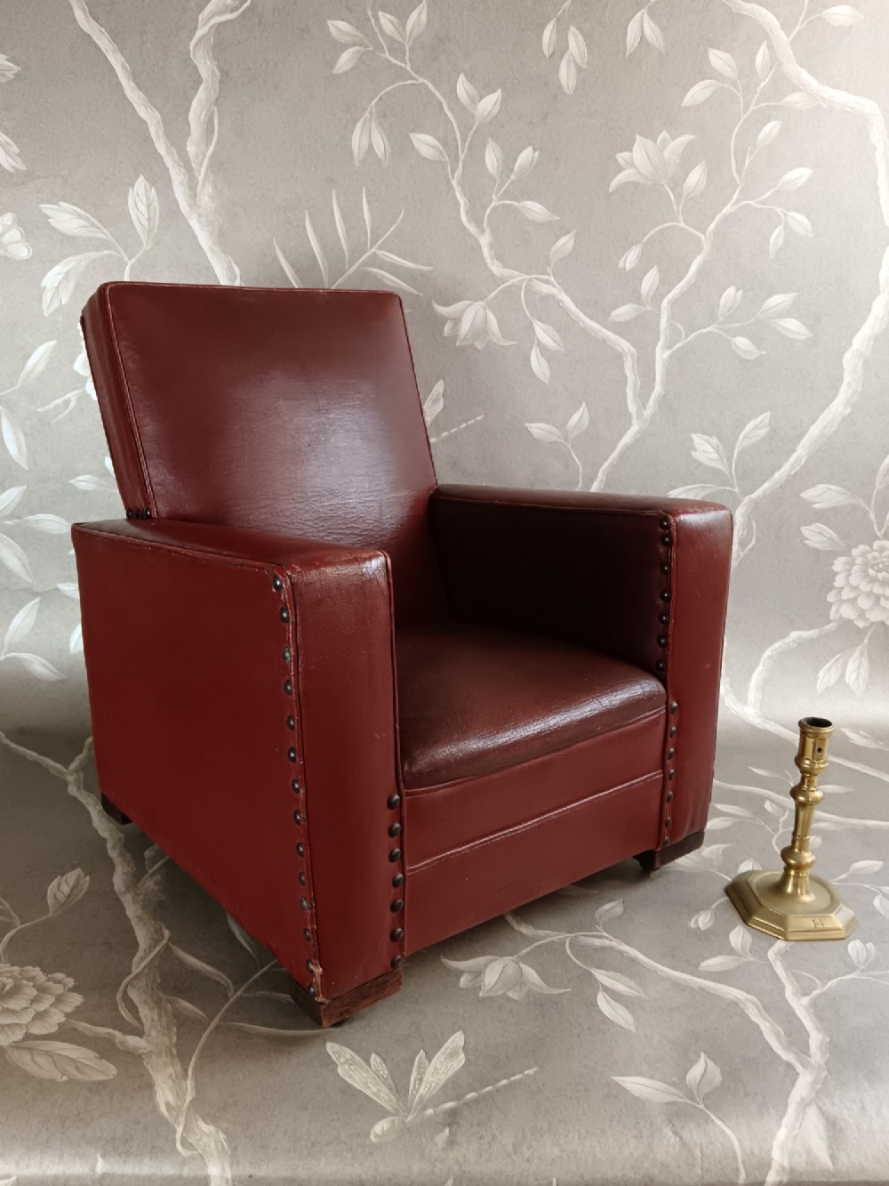A child-sized 1930s Art Deco club chair upholstered in oxblood red leather with studded trim along the arms.