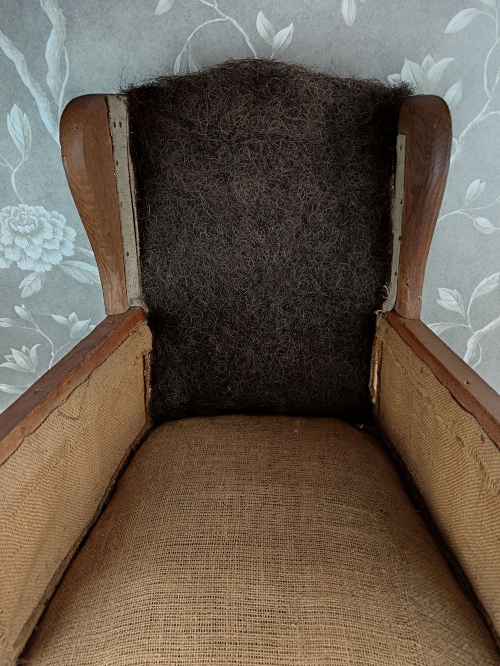 An early 20th-century childs wingback armchair featuring an exposed timber frame, tapered legs, and visible hessian upholstery layer. View XI