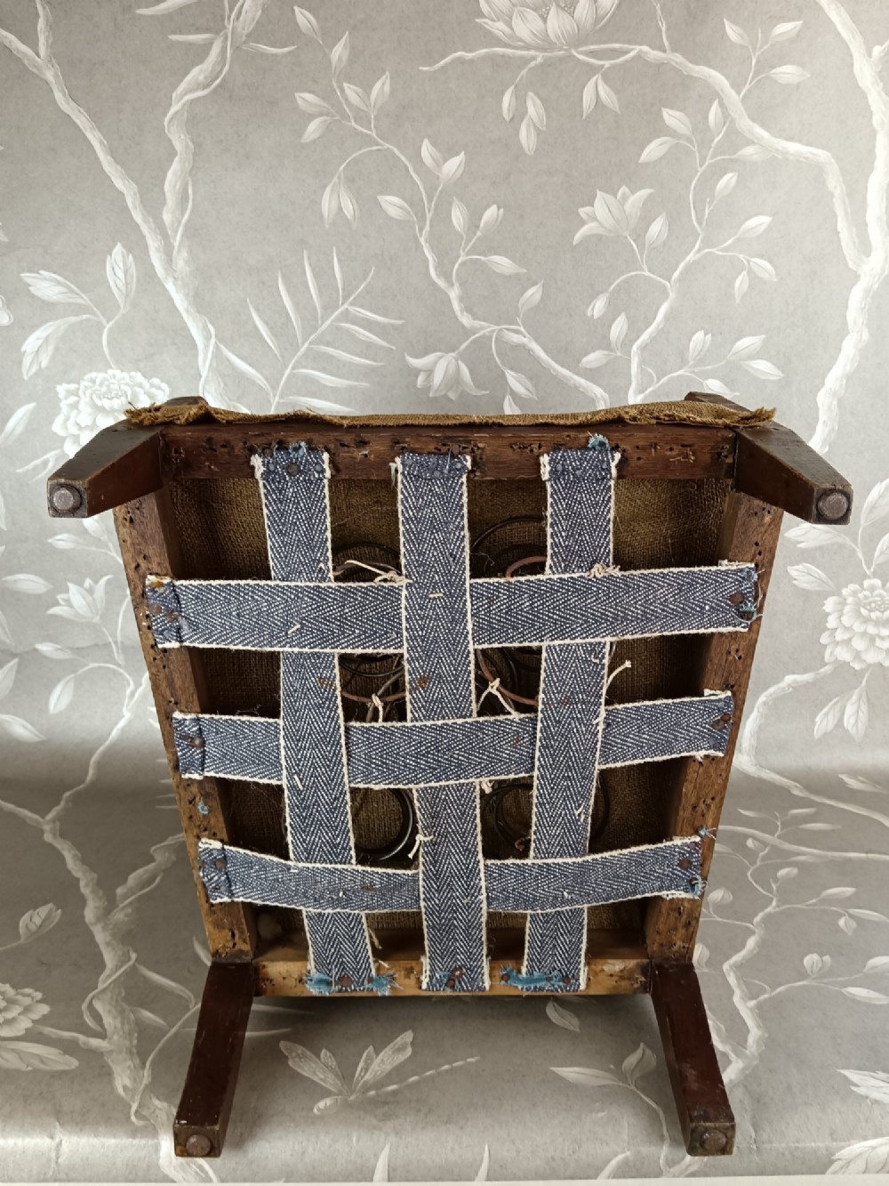An early 20th-century childs wingback armchair featuring an exposed timber frame, tapered legs, and visible hessian upholstery layer. View XII