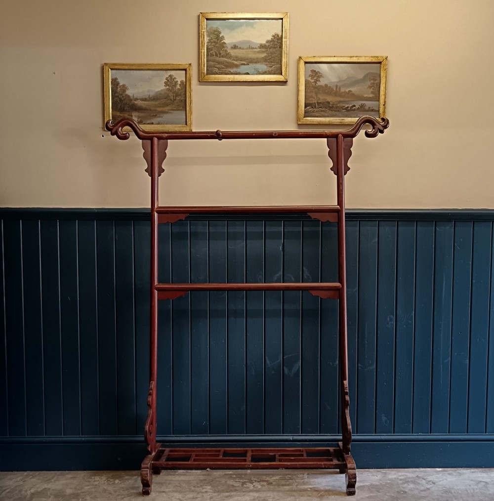 A late 19th-century Chinese red lacquered wooden robe stand with carved scroll terminals, horizontal crossbars, and a lower latticework base.