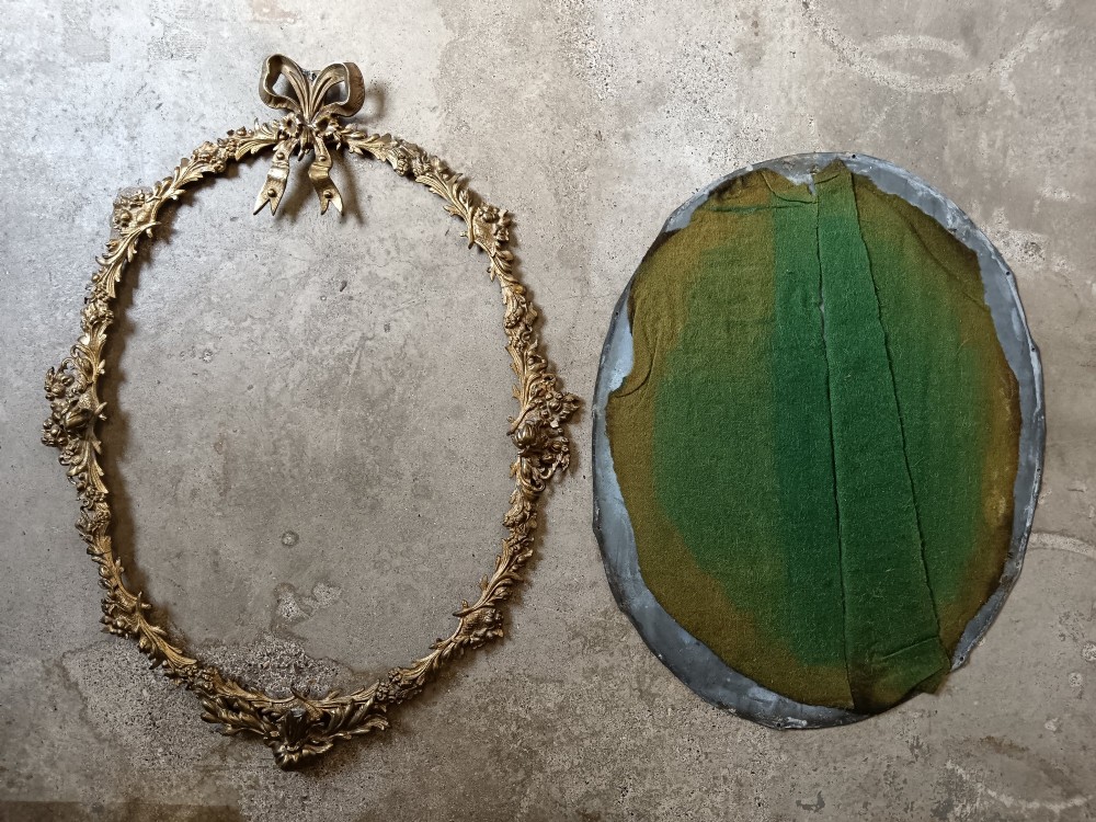 An oval wall mirror framed in detailed gilt bronze with floral scrollwork and a prominent ribbon bow crest at the top. View VIII