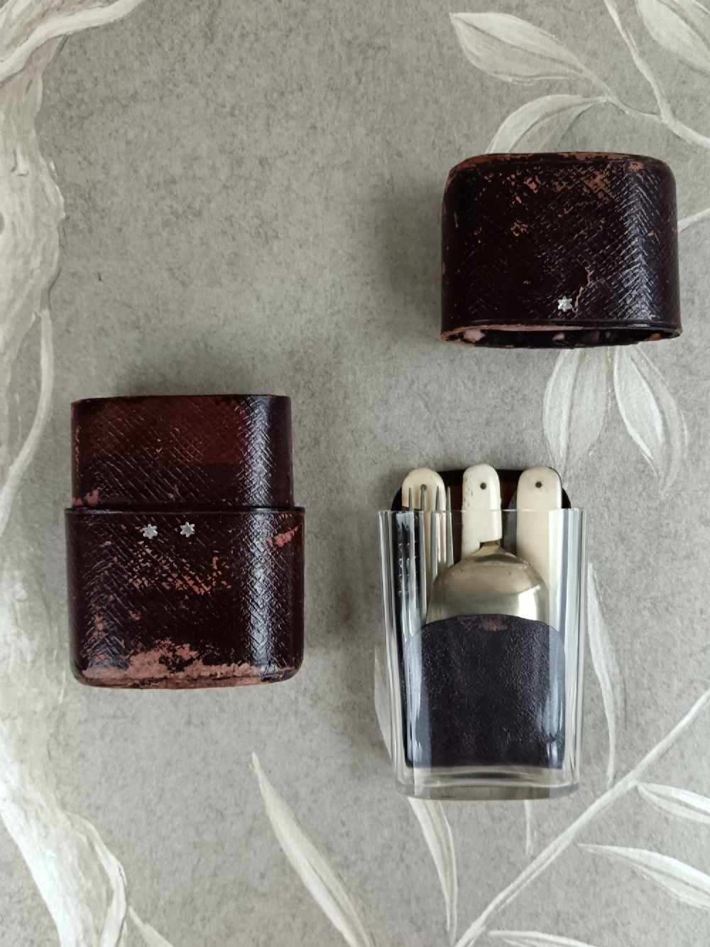 A Victorian folding campaign cutlery set featuring silver-plated utensils with light-coloured handles, a clear glass beaker, and a fitted dark red morocco leather carrying case. View III