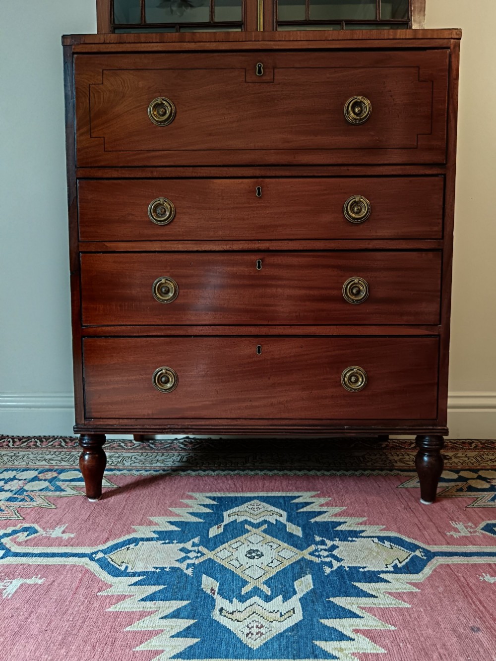 A Regency mahogany secretaire cabinet featuring a triangular pediment top, glazed upper doors, a fall-front desk section, and three drawers below on turned feet. View V