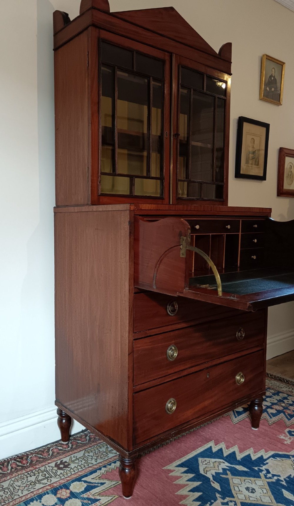 A Regency mahogany secretaire cabinet featuring a triangular pediment top, glazed upper doors, a fall-front desk section, and three drawers below on turned feet. View VIII