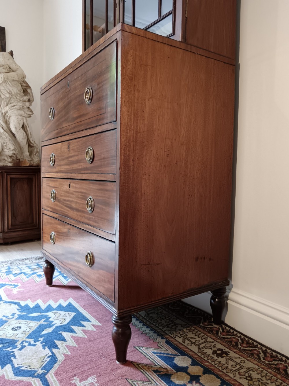 A Regency mahogany secretaire cabinet featuring a triangular pediment top, glazed upper doors, a fall-front desk section, and three drawers below on turned feet. View X