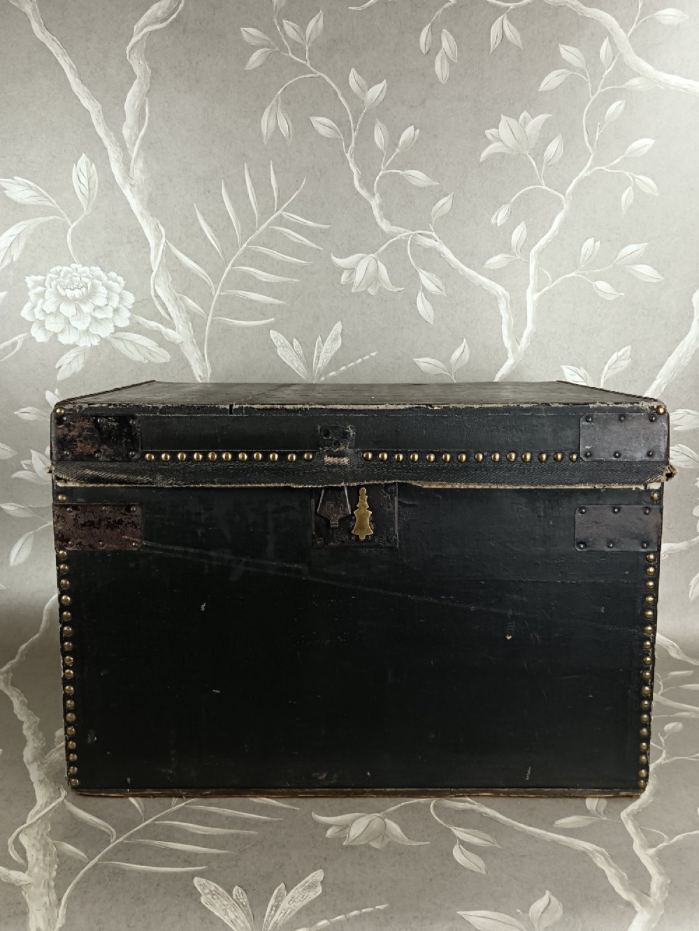 A rectangular black leather travelling trunk featuring brass stud border detail, iron corner reinforcement brackets, and a brass central lock escutcheon. View IX