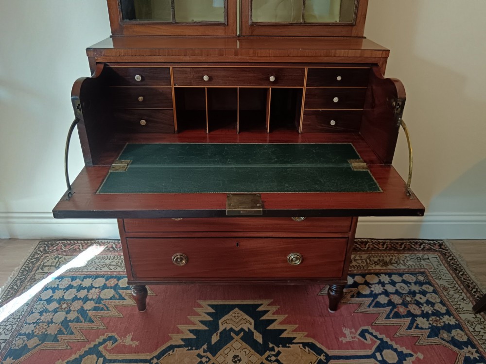 A Regency mahogany secretaire cabinet featuring a triangular pediment top, glazed upper doors, a fall-front desk section, and three drawers below on turned feet. View XII