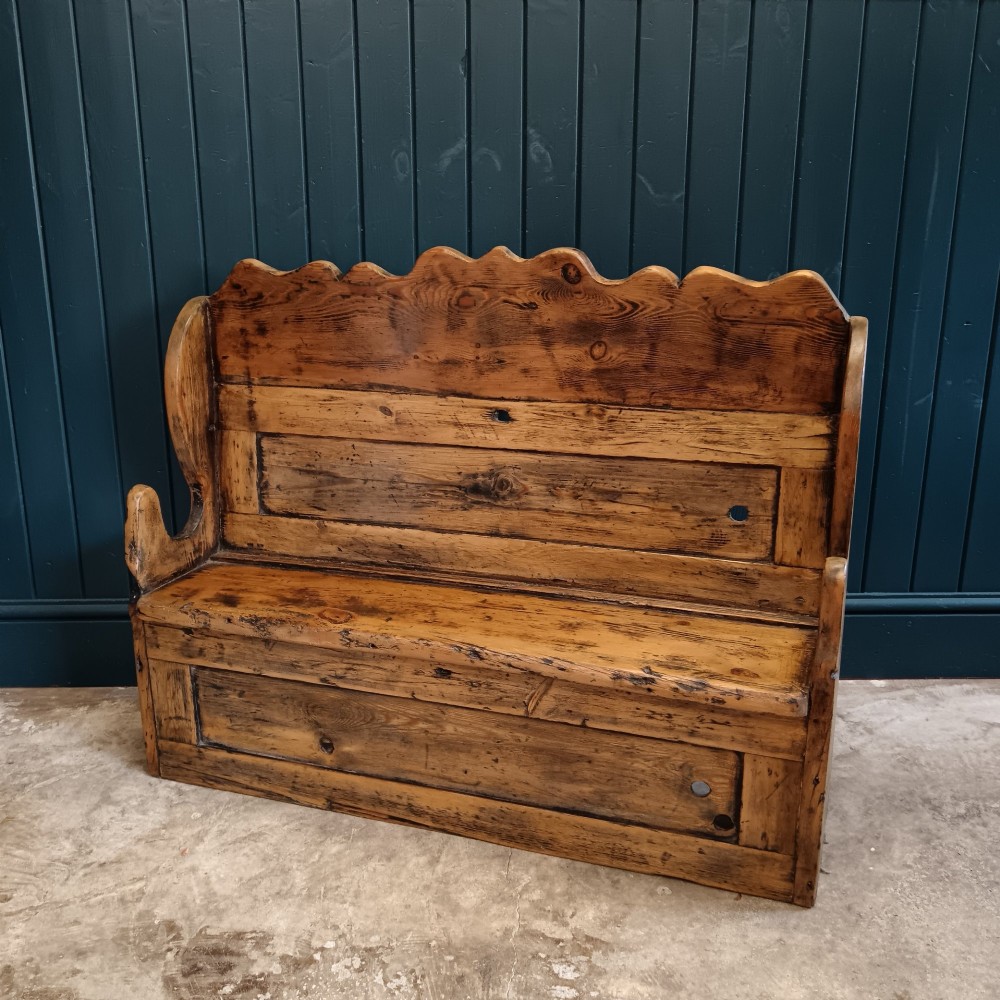An antique 19th-century country pine and elm settle bench with a high scalloped cresting rail and a warm brown waxed timber finish.