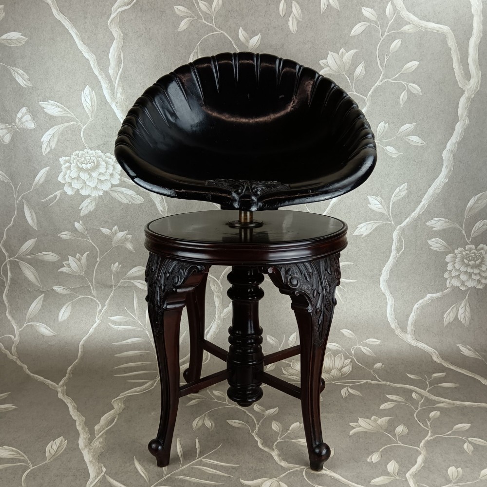 A Victorian mahogany revolving music stool with a scalloped shell-shaped black backrest, turned central pedestal, and four carved legs.