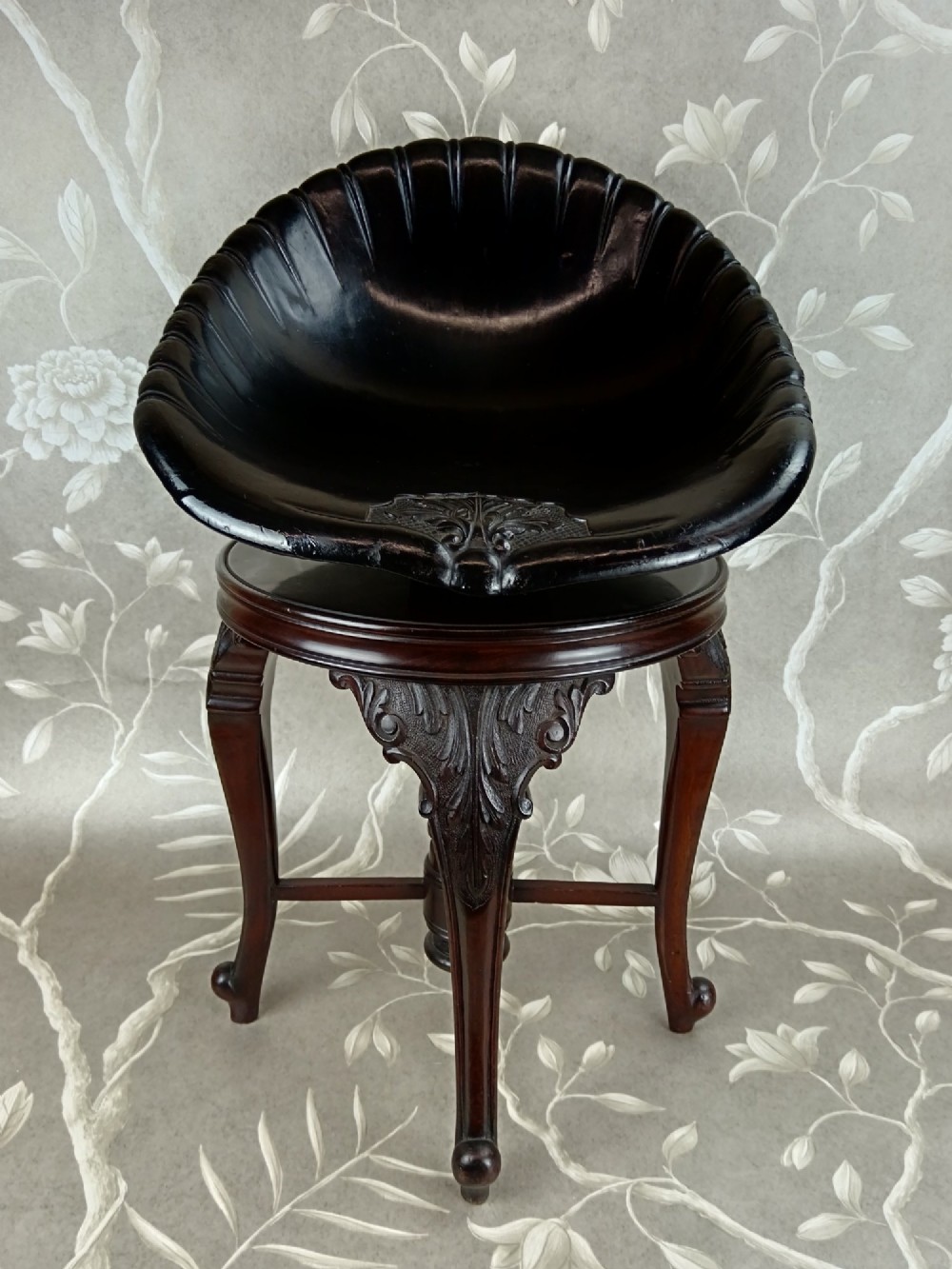 A Victorian mahogany revolving music stool with a scalloped shell-shaped black backrest, turned central pedestal, and four carved legs. View II