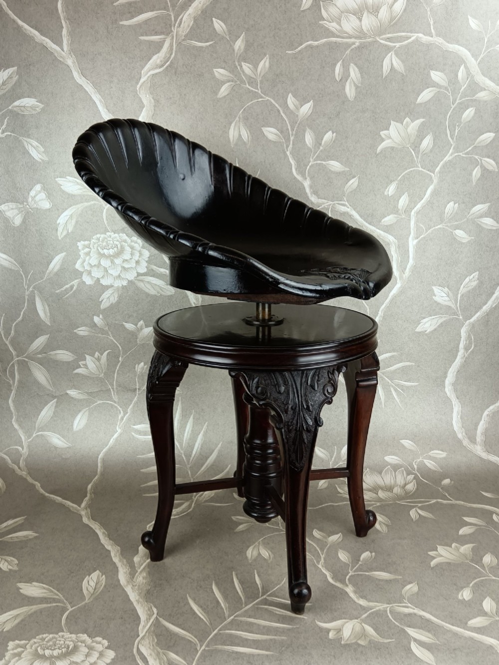 A Victorian mahogany revolving music stool with a scalloped shell-shaped black backrest, turned central pedestal, and four carved legs. View III
