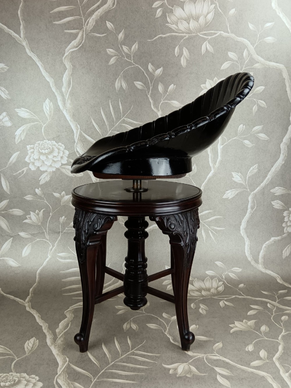 A Victorian mahogany revolving music stool with a scalloped shell-shaped black backrest, turned central pedestal, and four carved legs. View IV