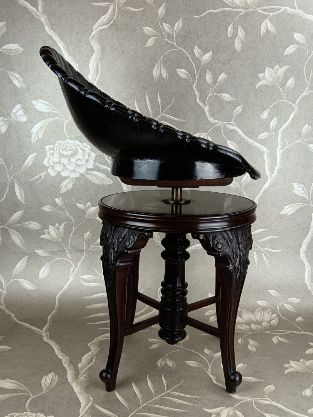 A Victorian mahogany revolving music stool with a scalloped shell-shaped black backrest, turned central pedestal, and four carved legs. View V