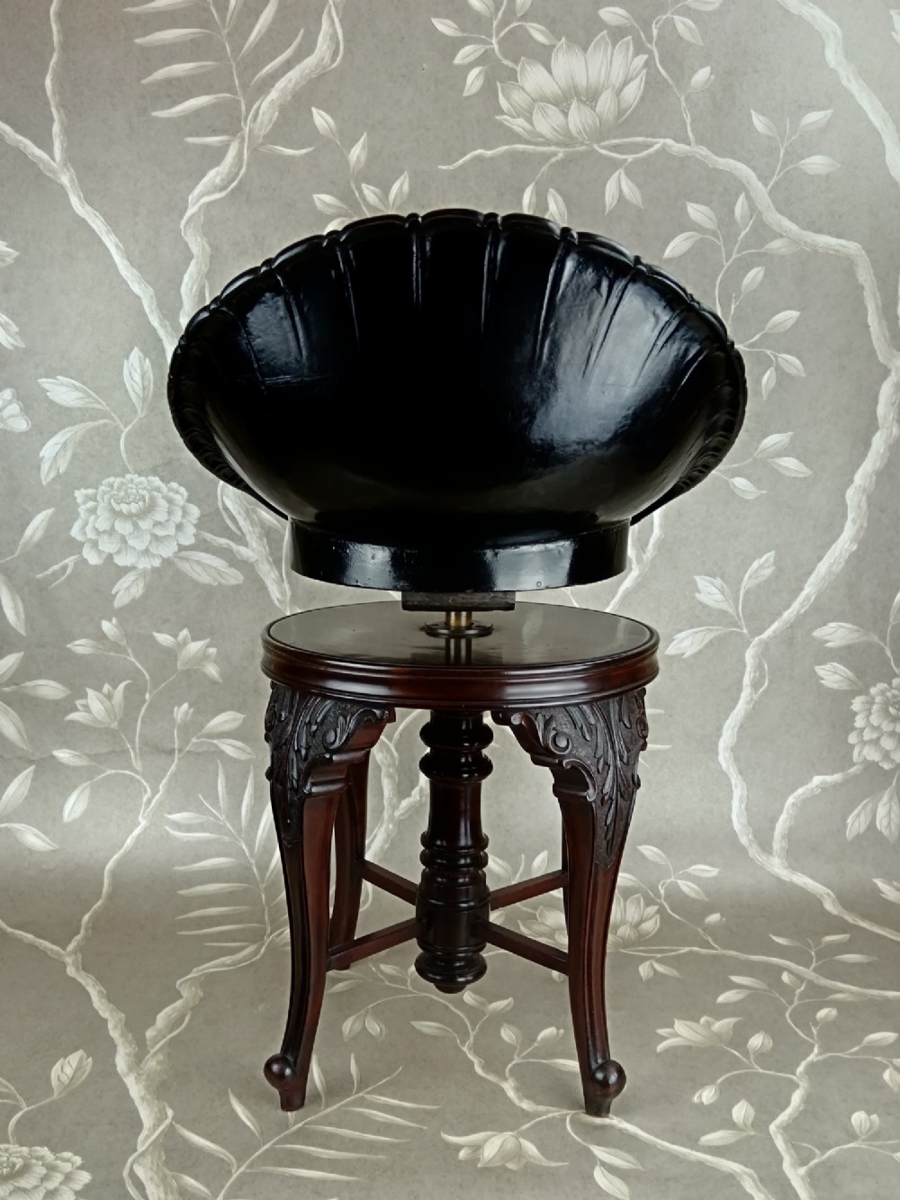A Victorian mahogany revolving music stool with a scalloped shell-shaped black backrest, turned central pedestal, and four carved legs. View VI