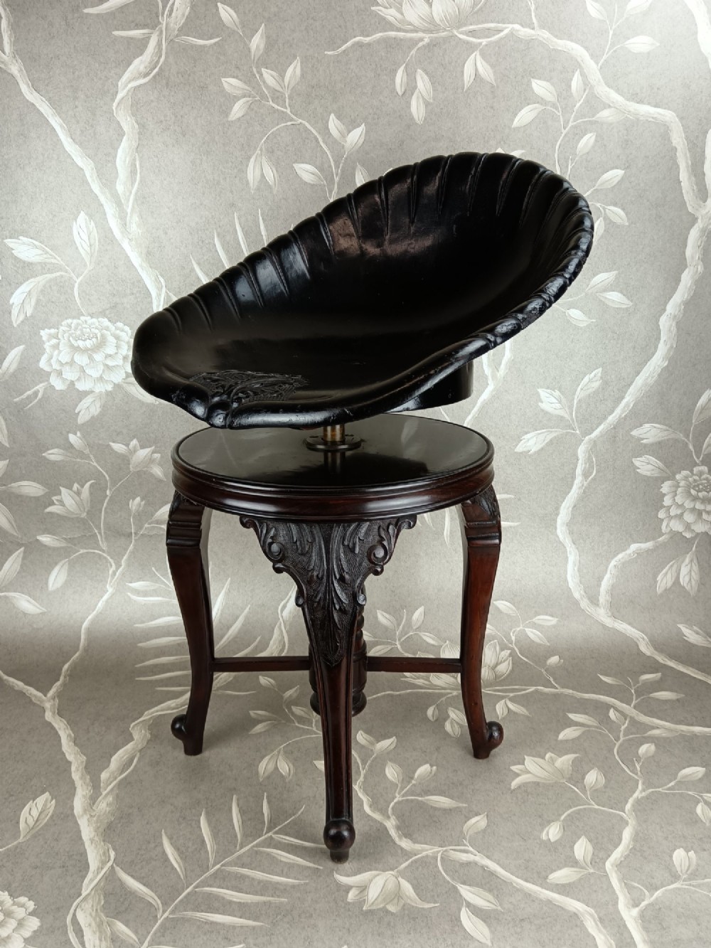 A Victorian mahogany revolving music stool with a scalloped shell-shaped black backrest, turned central pedestal, and four carved legs. View VII