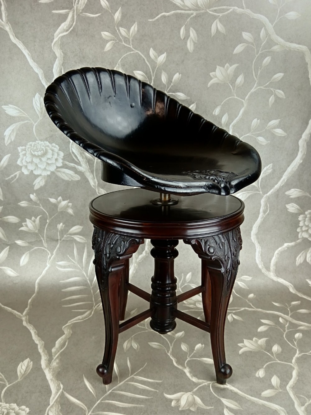 A Victorian mahogany revolving music stool with a scalloped shell-shaped black backrest, turned central pedestal, and four carved legs. View VIII