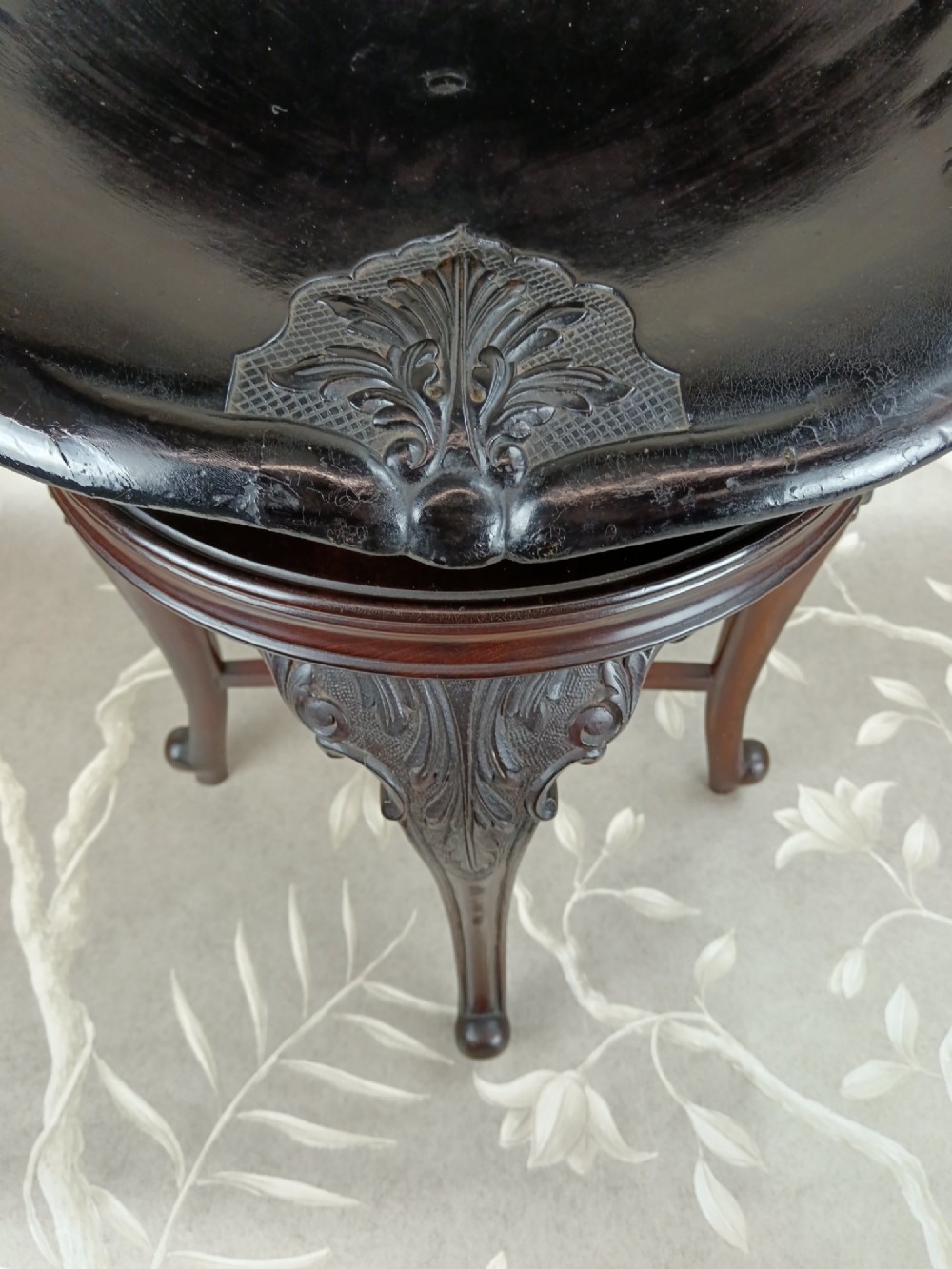 A Victorian mahogany revolving music stool with a scalloped shell-shaped black backrest, turned central pedestal, and four carved legs. View IX