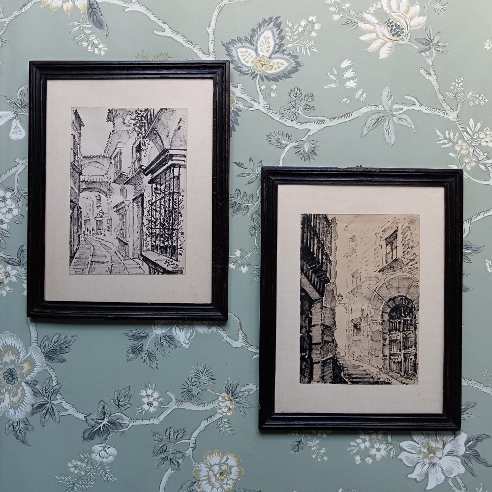 A pair of framed mid-century black ink architectural drawings depicting narrow Spanish street scenes mounted in dark wooden frames.
