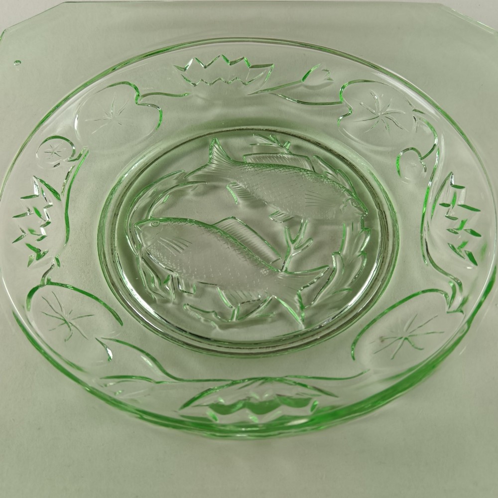 A square pale green Art Deco pressed glass plate featuring a central circular design of two swimming fish surrounded by embossed water lilies. View II