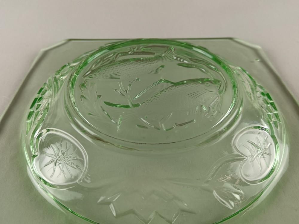 A square pale green Art Deco pressed glass plate featuring a central circular design of two swimming fish surrounded by embossed water lilies. View VI