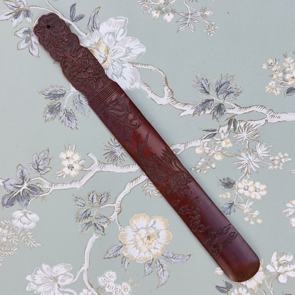 A long, flat carved bamboo page turner featuring relief carvings of a carp, figure, and floral details in a dark reddish-brown finish.