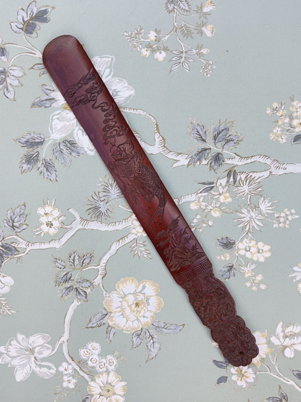 A long, flat carved bamboo page turner featuring relief carvings of a carp, figure, and floral details in a dark reddish-brown finish. View II