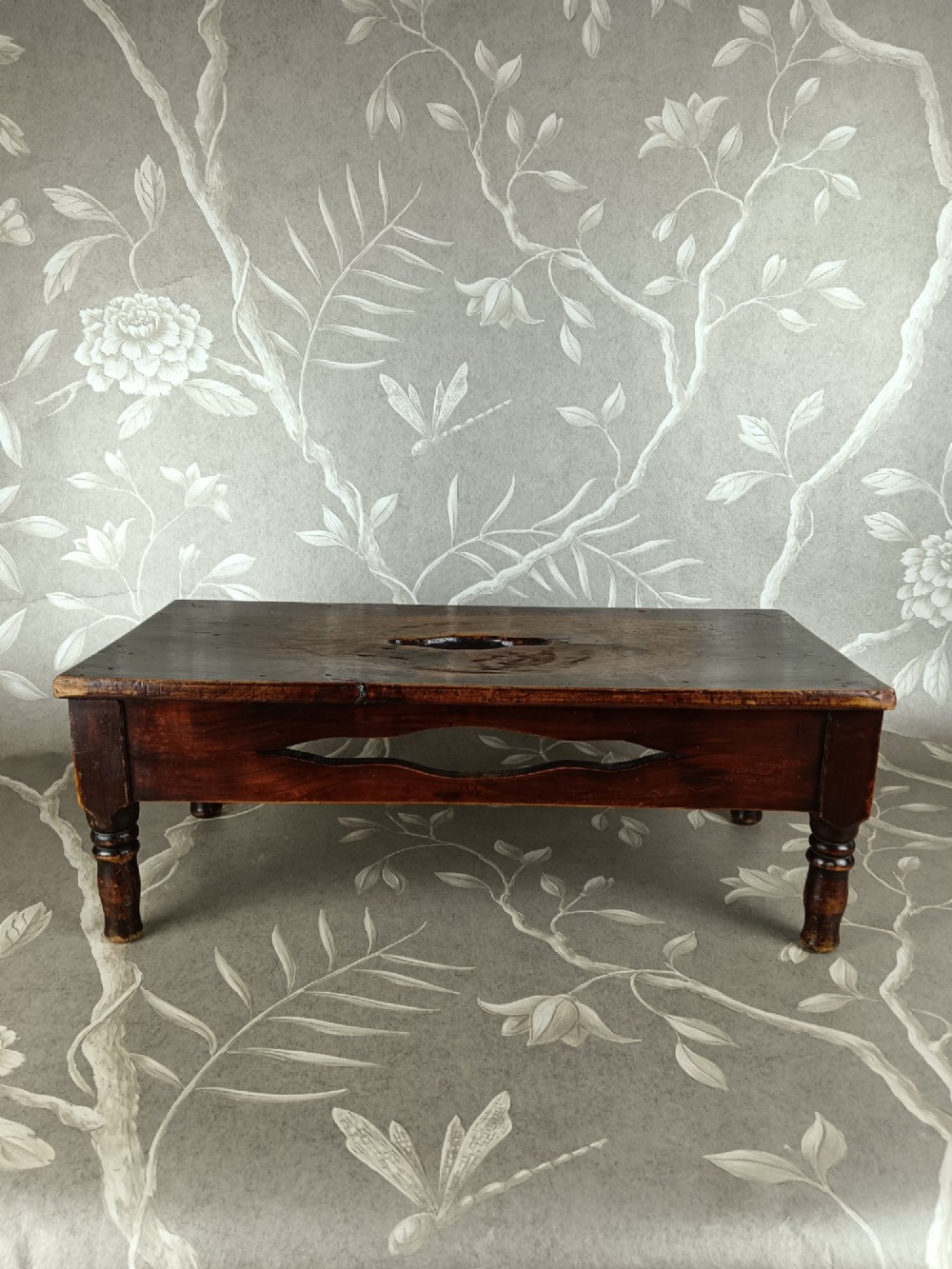 A low 19th-century dark brown wooden footstool with turned legs, side cutouts, and a central carry handle slot on the top surface. View IV