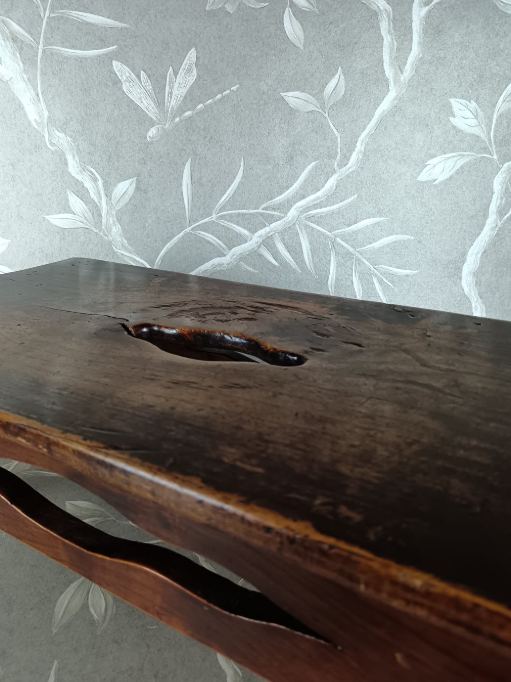 A low 19th-century dark brown wooden footstool with turned legs, side cutouts, and a central carry handle slot on the top surface. View VII