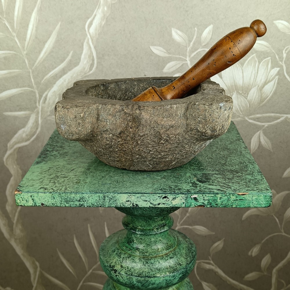 An antique hand-carved stone mortar featuring four corner lugs, shown with a turned fruitwood pestle.