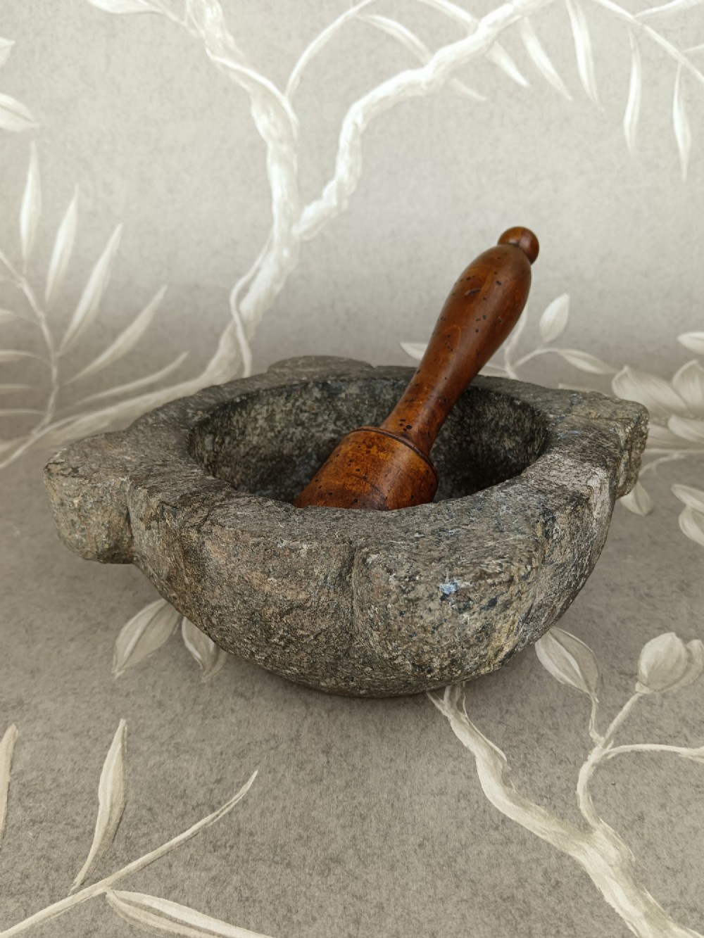 An antique hand-carved stone mortar featuring four corner lugs, shown with a turned fruitwood pestle. View II